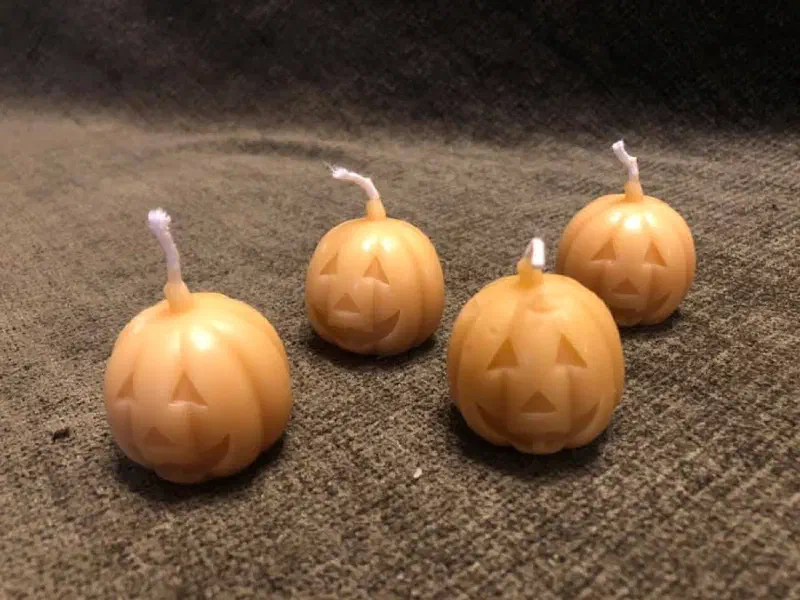 Four small beeswax candles shaped like carved Halloween pumpkins