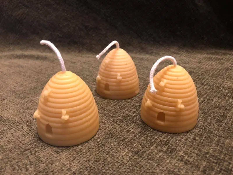 Three beeswax candles shaped like traditional straw bee skeps, with tiny bees on the sides