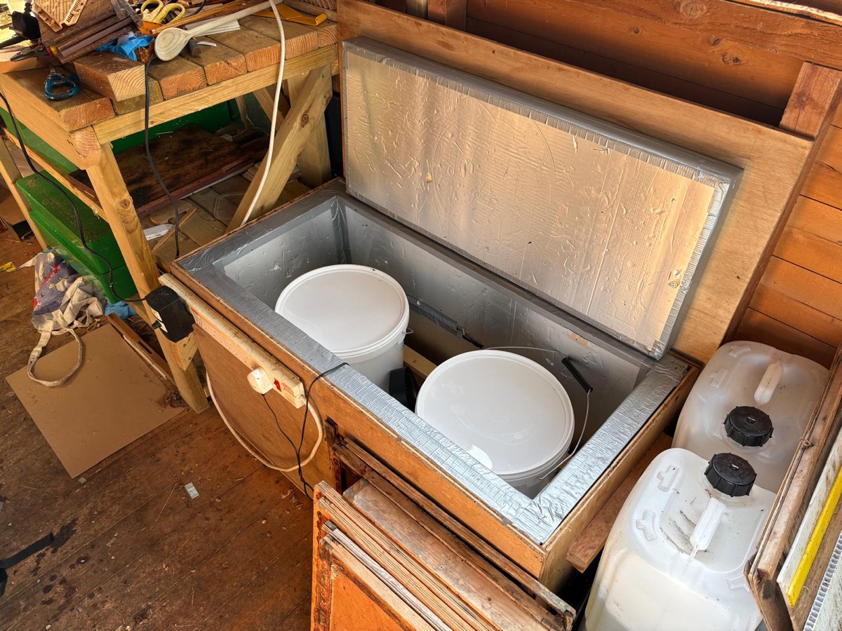 Two honey buckets inside a wooden insulated honey warmer, lid open